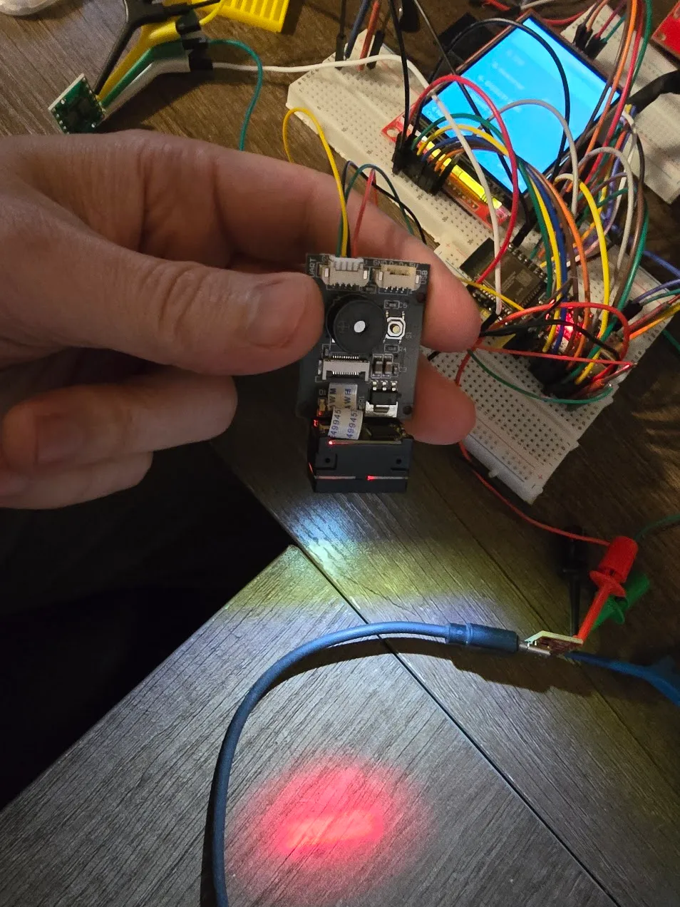 GM65 barcode scanner module held in hand with its red aiming line lit on the desk