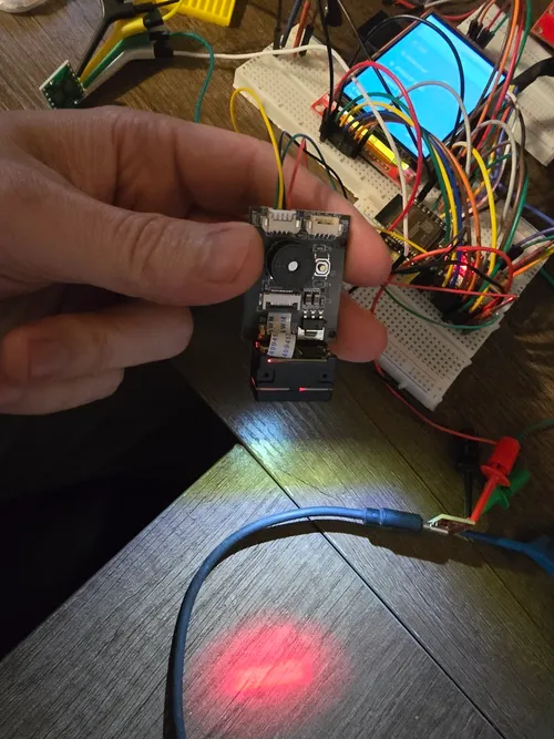 GM65 barcode scanner module held in hand with its red aiming line and illumination lit up on the desk